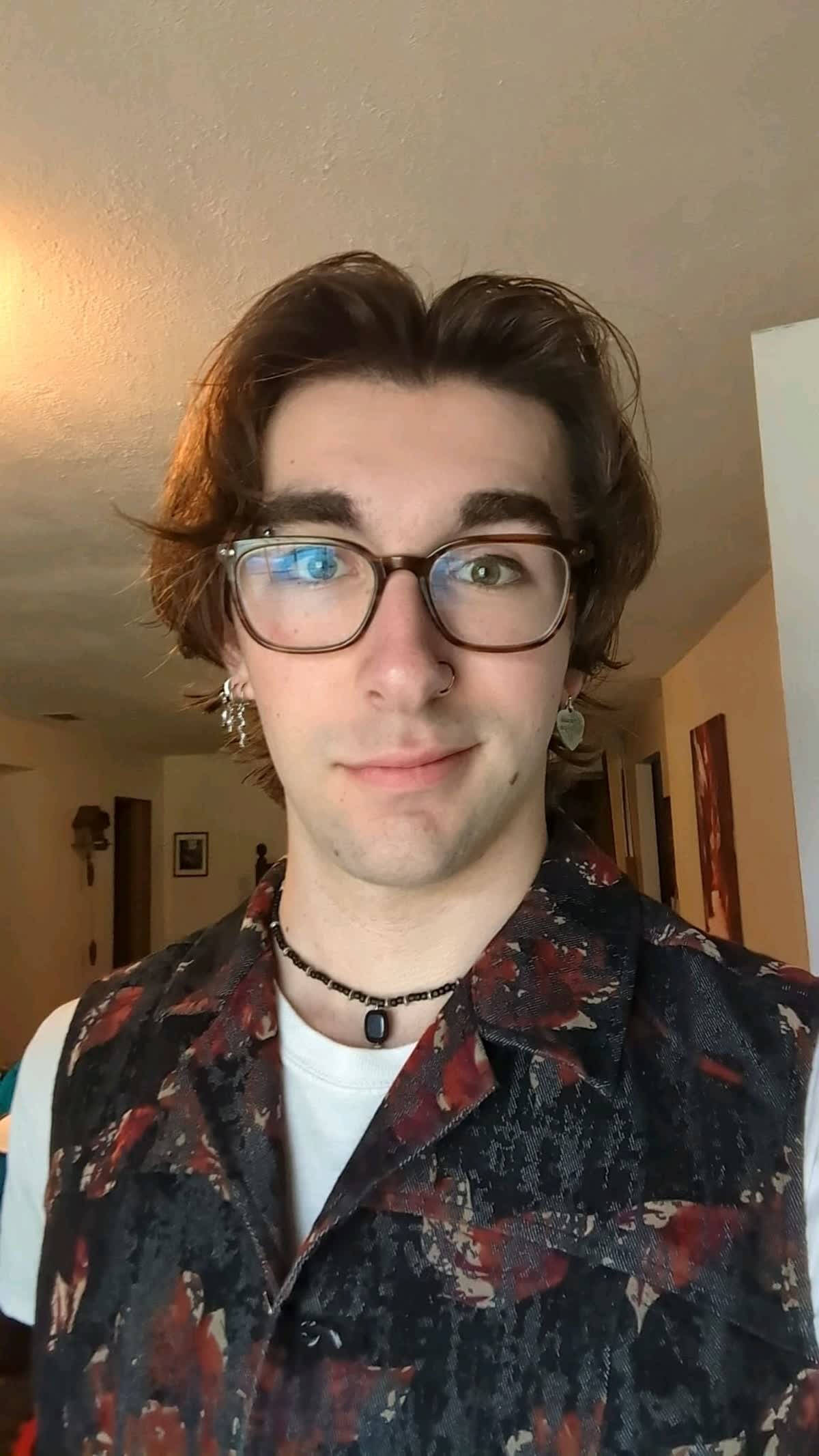 Andrew in dark-rimmed glasses with a pendant necklace and dark, patterned vest